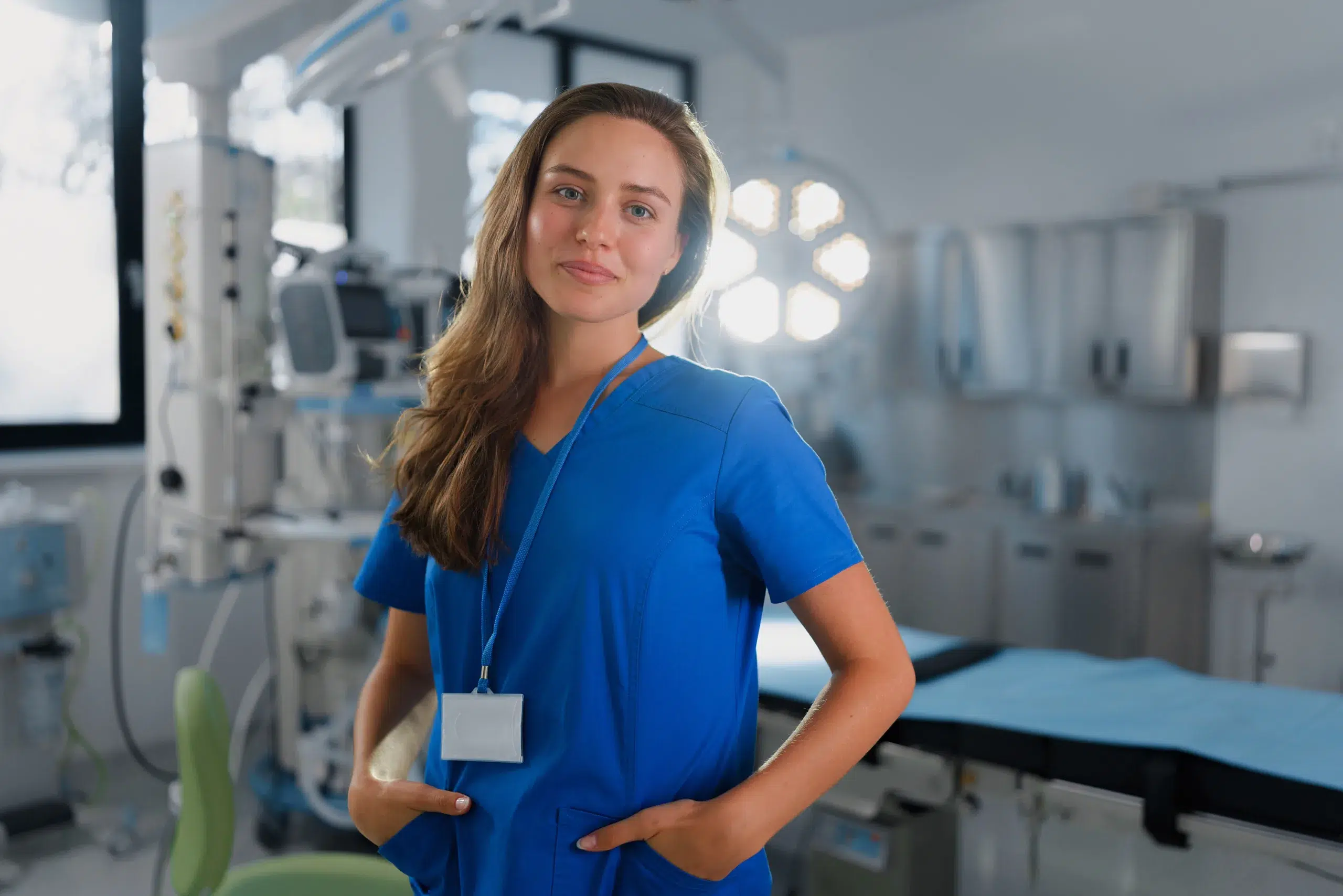 A woman in blue medical scrubs stands confidently in a bright, modern hospital room—an ideal image for marketing to nurses.