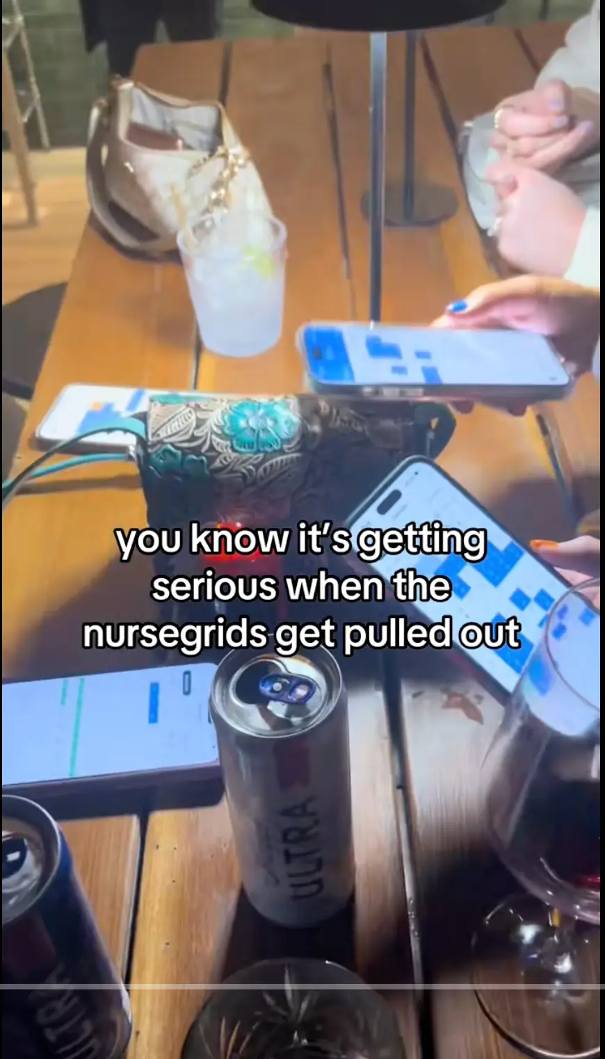 Three people sit at a table with drinks, holding phones showing schedules. Text overlay reads, you know its getting serious when the nursegrids get pulled out.